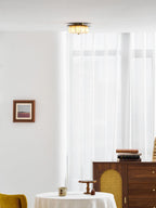 A Clérachic fabric ceiling light above a white room with a rattan-fronted walnut cabinet, books and a framed print.