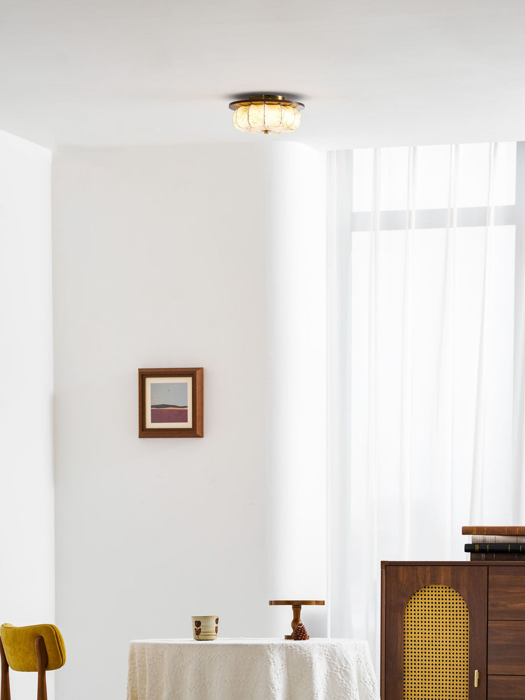 A Clérachic fabric ceiling light seen from afar above a round table, with a framed print and a walnut cabinet.