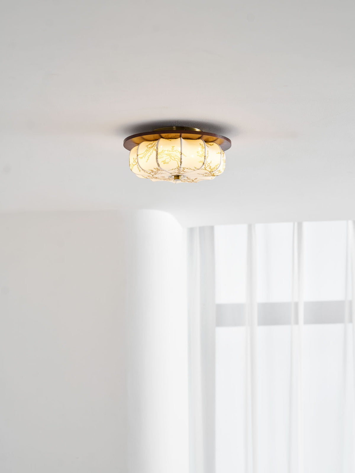 A lit Clérachic ceiling light with a floral-etched fabric shade and a walnut rim, near a window with sheer curtains.