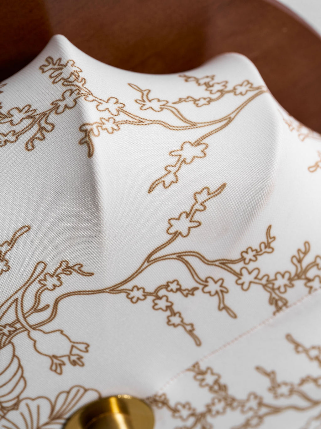 Close view of the gold-toned floral line pattern on the fabric shade of this Clérachic ceiling light, beside its brass cap.