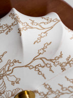 Close view of the gold-toned floral line pattern on the fabric shade of this Clérachic ceiling light, beside its brass cap.