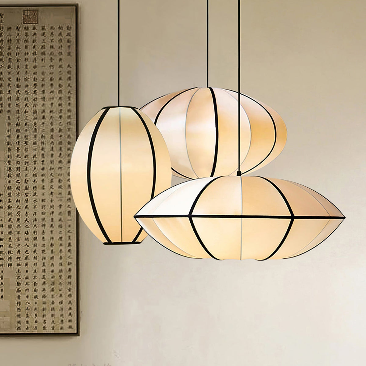 Three lit fabric pendants in different shapes hang together beside a framed calligraphy scroll, their black ribbing clear, from Clérachic.