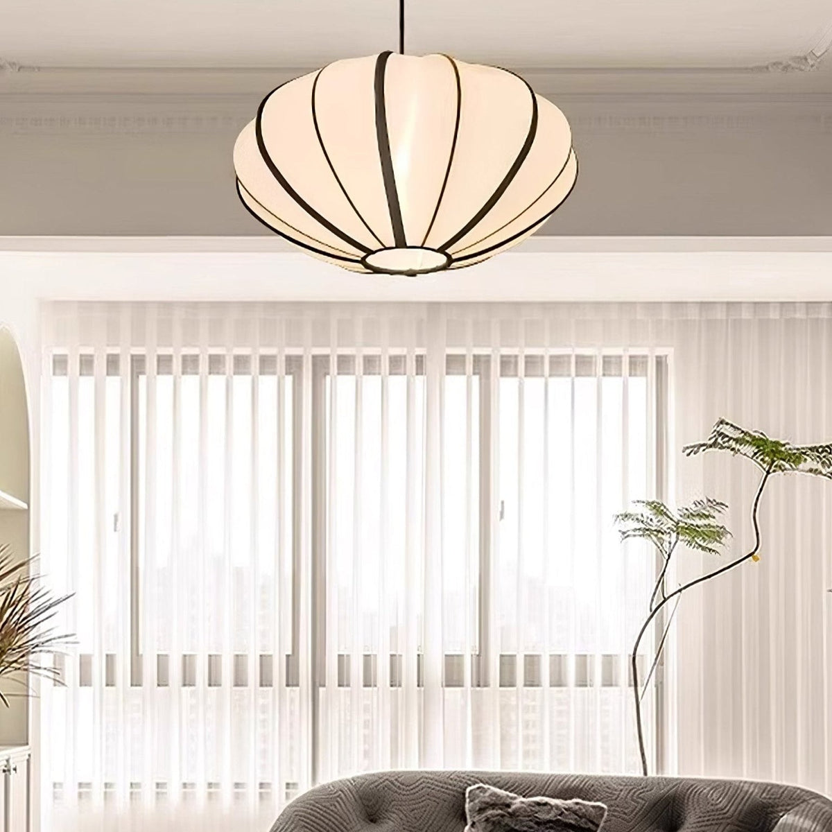 A ribbed fabric pendant sits flush to a moulded ceiling in a living room with sheer vertical blinds and a grey sofa, from Clérachic.