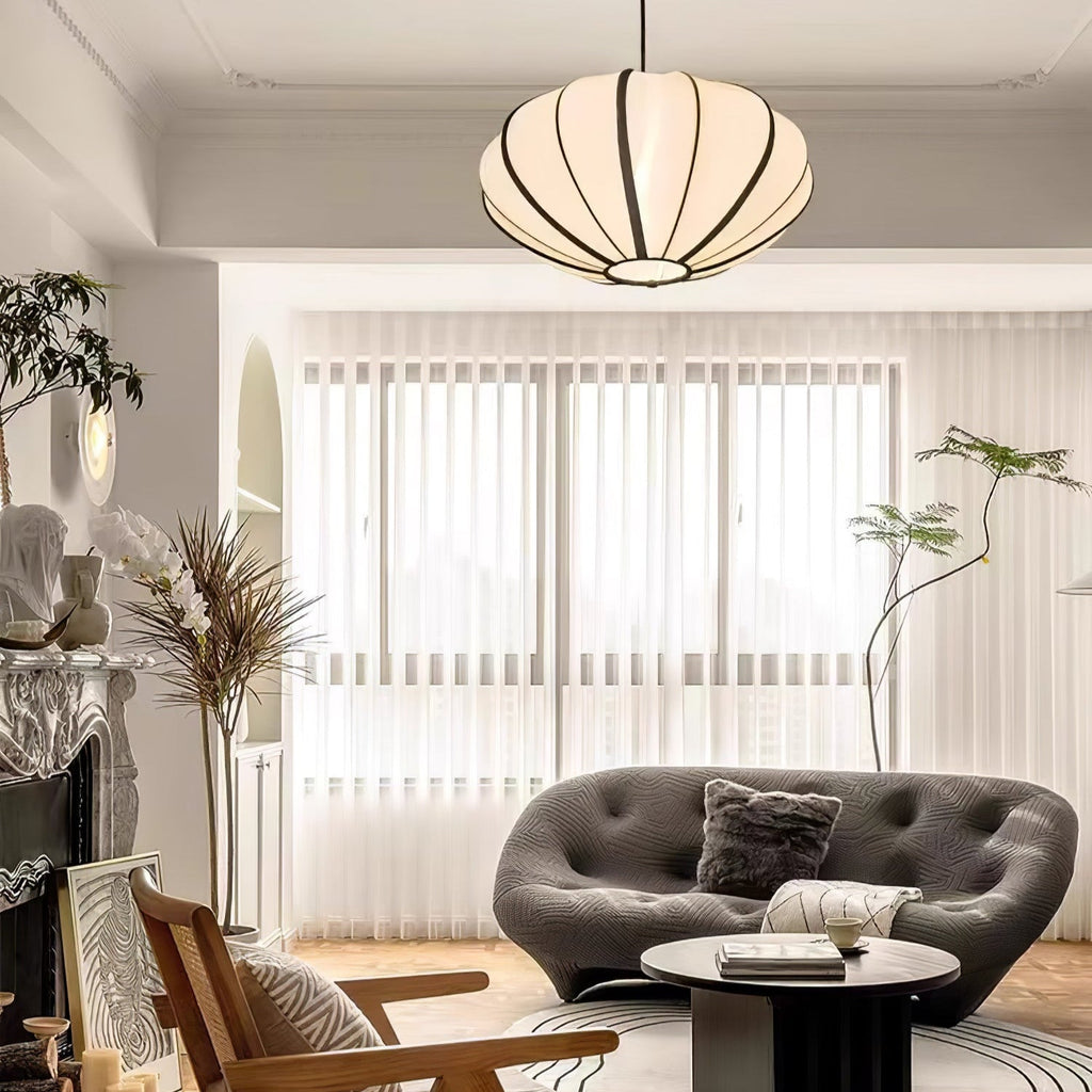 A fabric pendant with black ribs hangs close to the ceiling in a bright living room with a grey sofa and sheer blinds, from Clérachic.