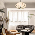 A fabric pendant with black ribs hangs close to the ceiling in a bright living room with a grey sofa and sheer blinds, from Clérachic.