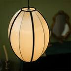 Close view of a tall egg-shaped fabric pendant with black ribs, lit from within, against a dark green background, from Clérachic.