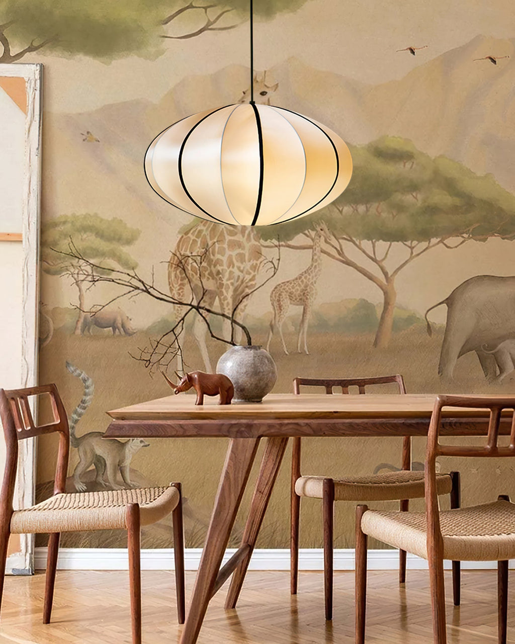 A ribbed fabric pendant hangs above a wooden dining table and rattan chairs, in front of a safari-animal mural, from Clérachic.