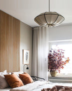 A white, scalloped fabric pendant with black ribs hangs above a bed with rust cushions, beside a timber-slat wall, from Clérachic.