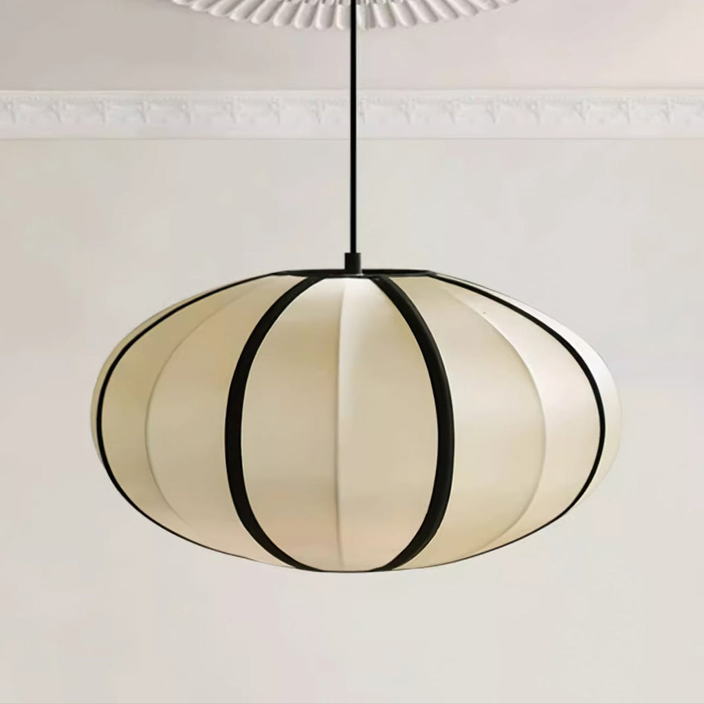 A flattened fabric pendant with bold black ribs hangs from a black cord, a moulded ceiling above, a wide Clérachic shade.