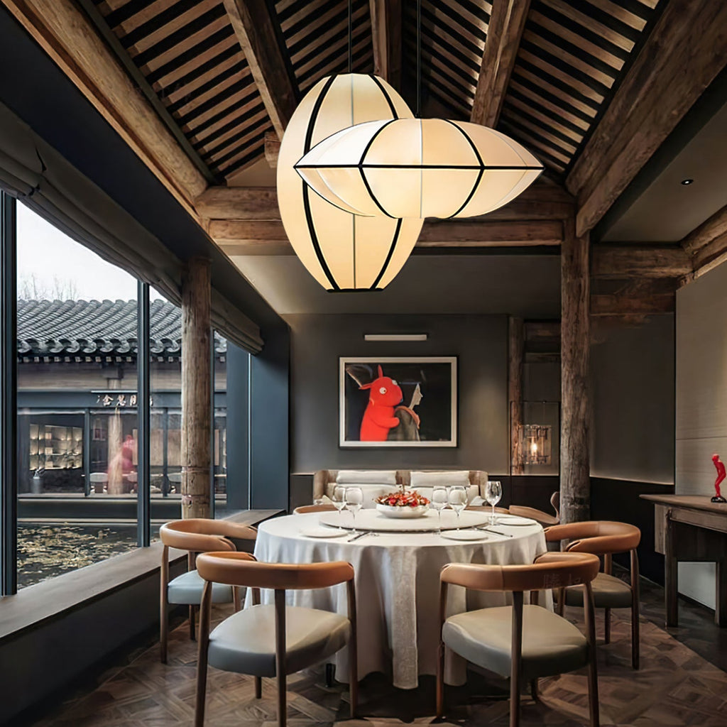 Two lit fabric pendants, one oval and one pointed, hang under a dark timber roof above a round dining table, from Clérachic.