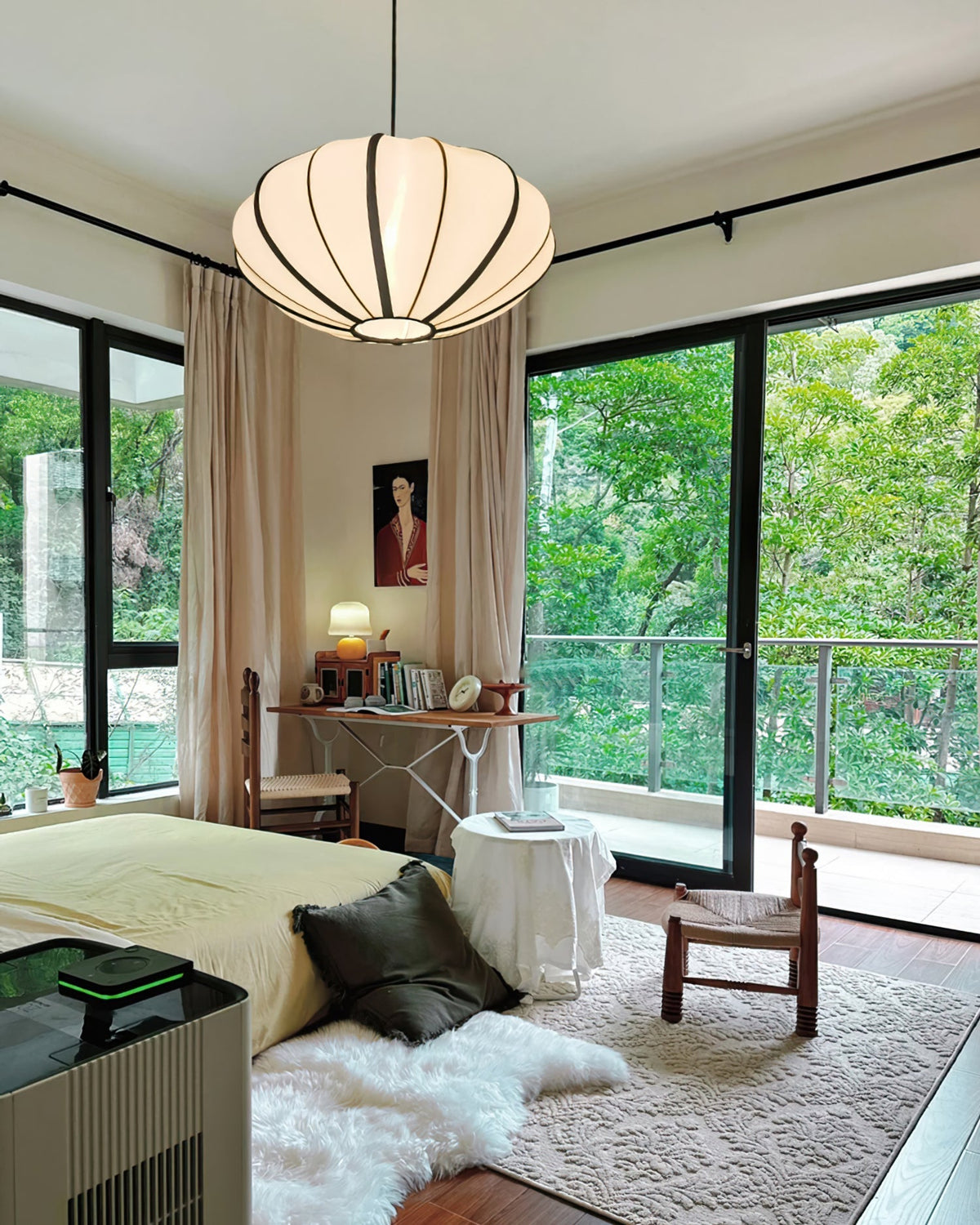 A ribbed fabric pendant hangs in a bedroom with floor-to-ceiling glass doors onto trees, above a bed and a fur rug, from Clérachic.