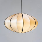 A rounded fabric pendant with black ribs and a warm glow hangs on a black cord against a plain grey backdrop, from Clérachic.