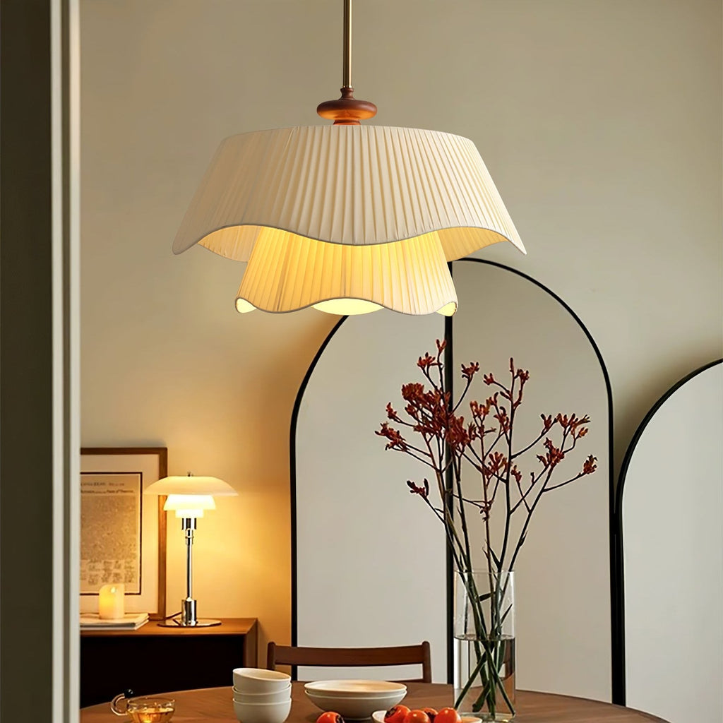 Lit Clérachic pendant with a ruffled pleated shade, hung above a round dining table beside an arched mirror and a vase of red stems.