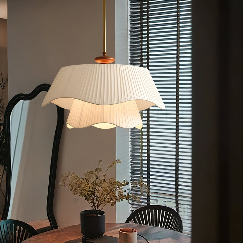 Wavy-edged Clérachic pendant glowing softly over a dining table, with a dark scalloped mirror and slatted blinds behind it.