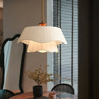 Wavy-edged Clérachic pendant glowing softly over a dining table, with a dark scalloped mirror and slatted blinds behind it.