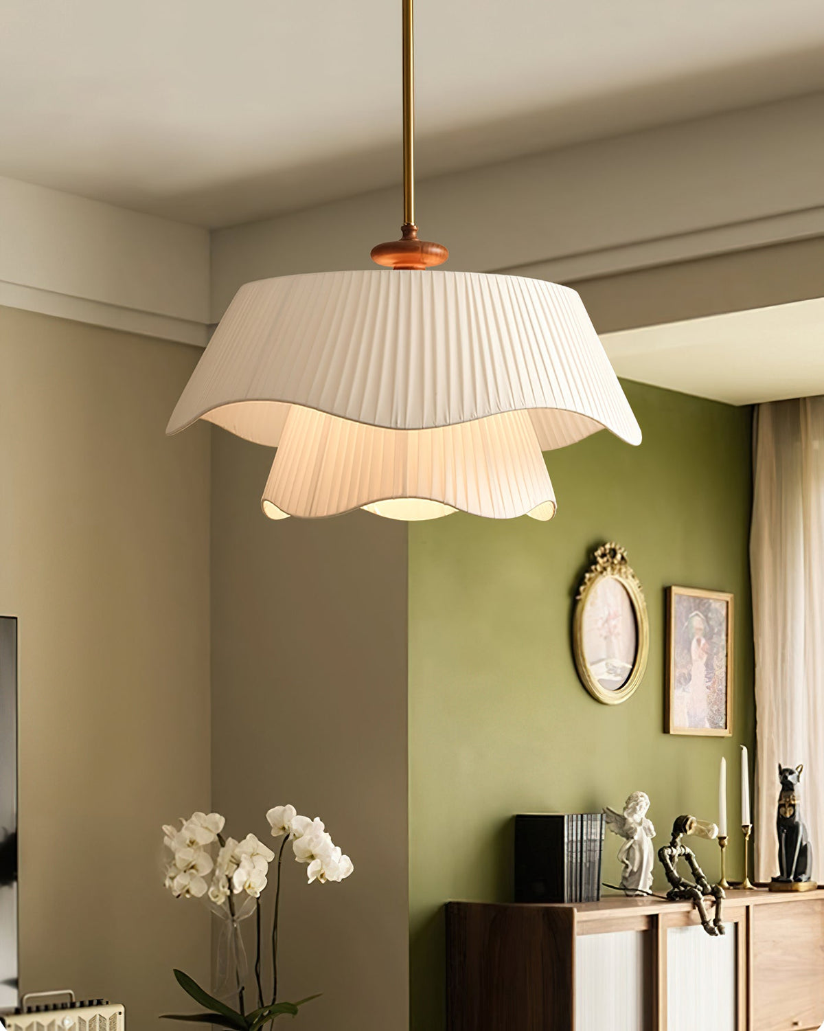 Clérachic pendant lit in a room with olive-green walls, a small oval mirror, white orchids and a sideboard below.