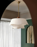 Reflected in an arched mirror, this Clérachic pendant hangs by its gold stem against sheer curtains and a deep green wall.