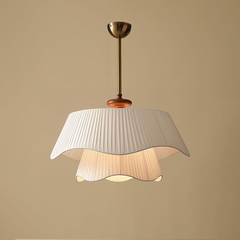 Unlit Clérachic pendant on a warm sand backdrop, showing the pleated outer shade, the wooden bead and the gold canopy.