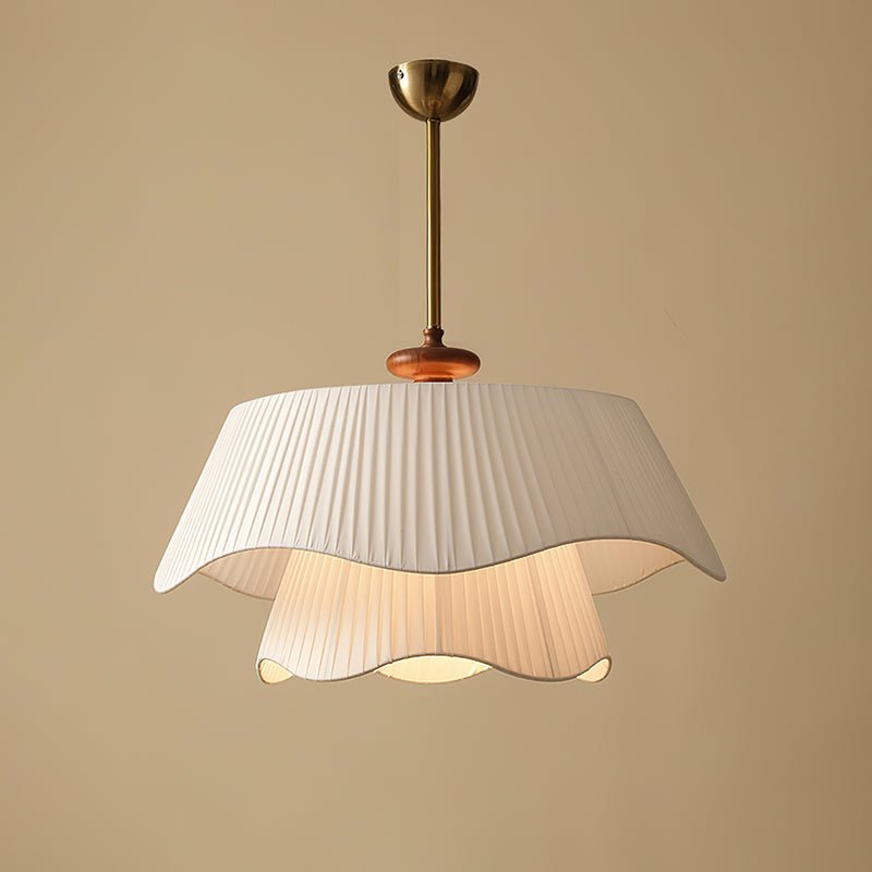 Wide view of the Clérachic pendant on a sand-coloured wall, the ruffled upper shade lit softly from within.