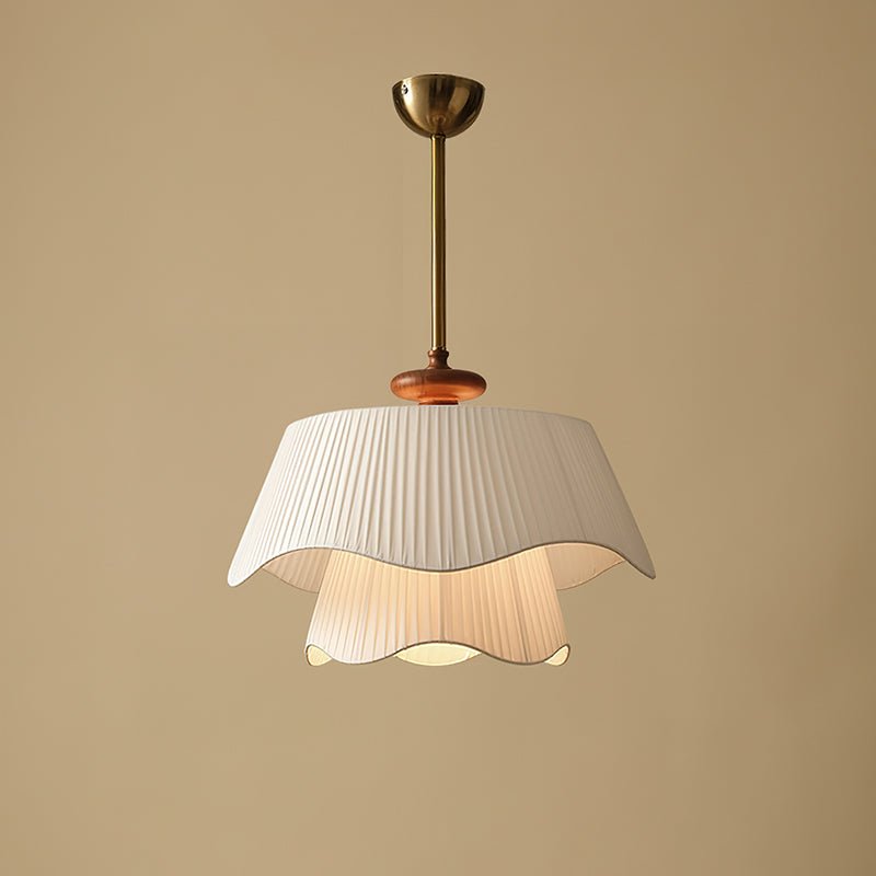 Straight-on view of the Clérachic pendant switched on, its two wavy fabric layers glowing gently against a plain beige wall.