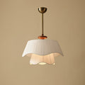 Straight-on view of the Clérachic pendant switched on, its two wavy fabric layers glowing gently against a plain beige wall.