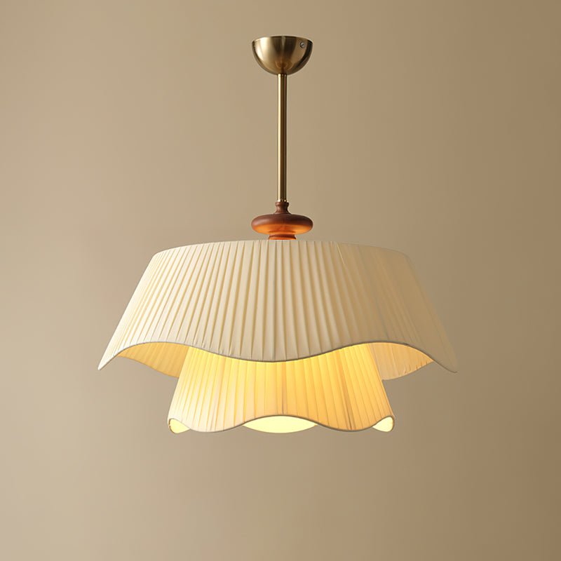 This Clérachic pendant lit warm amber on a beige backdrop, the ruffled edge of the pleated shade casting light downward.
