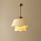 Lit Clérachic pendant on a plain beige wall, its inner fabric layer glowing a warm yellow beneath the wavy outer shade.