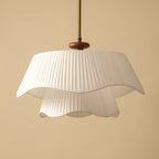 Close view of the pleated fabric folds and wavy hem on this Clérachic pendant, with its dark wooden bead and gold stem.