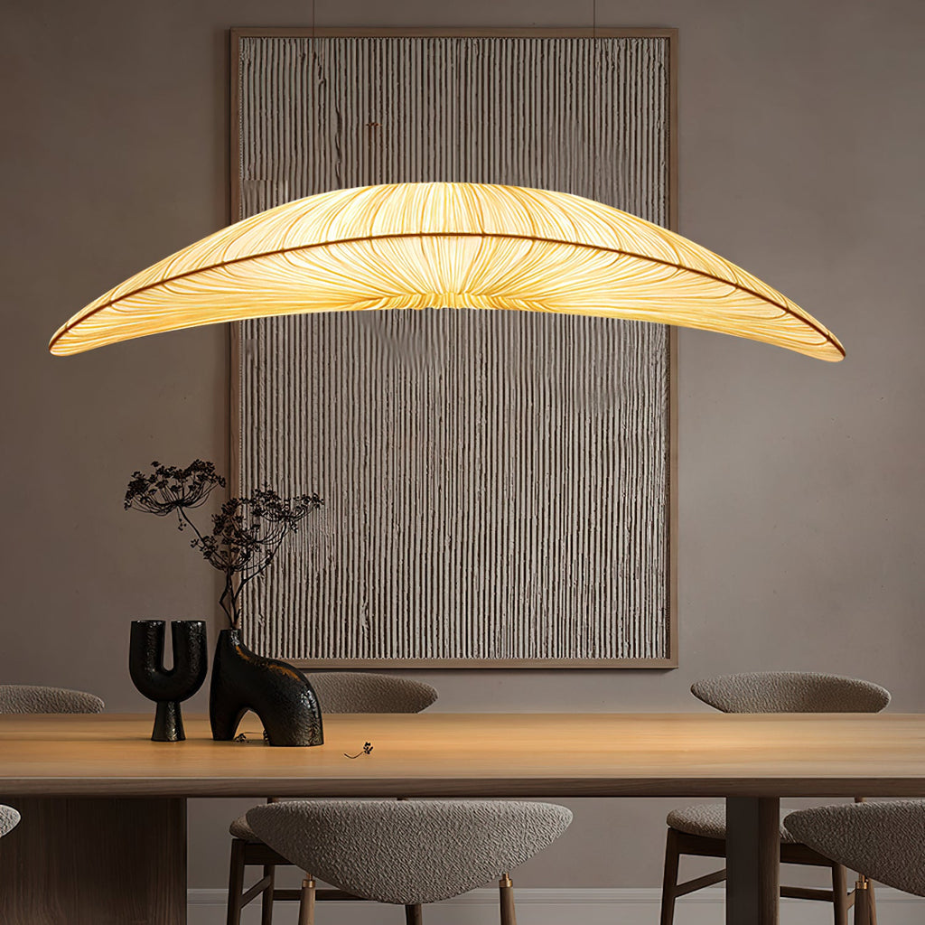 Over a wooden table with a dark vase, a Clérachic pendant with a long pleated shade hangs in front of a ridged wall panel.