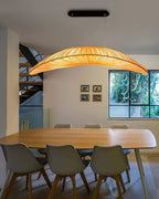A Clérachic leaf-shaped pendant hangs over a light wooden dining table with grey chairs, near an open staircase and a window.