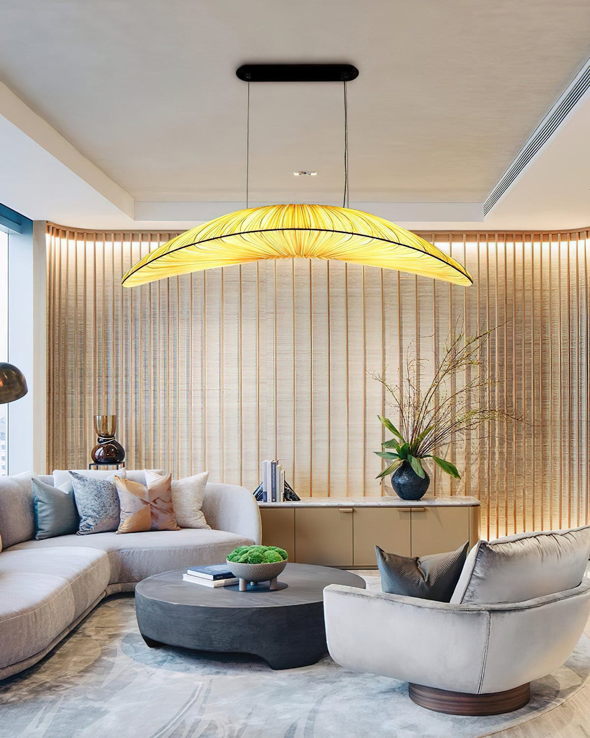 A Clérachic pendant with a bright pleated shade hangs above a cream sofa and low round table, in front of a slatted wooden wall.