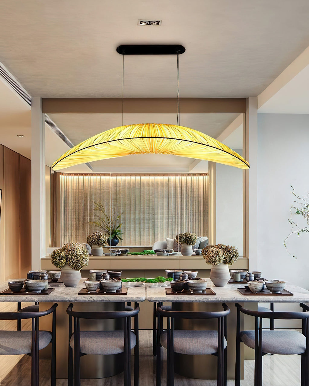A Clérachic pendant lights a long dining table set with bowls and dishes, in a room with a softly lit wooden slatted wall.