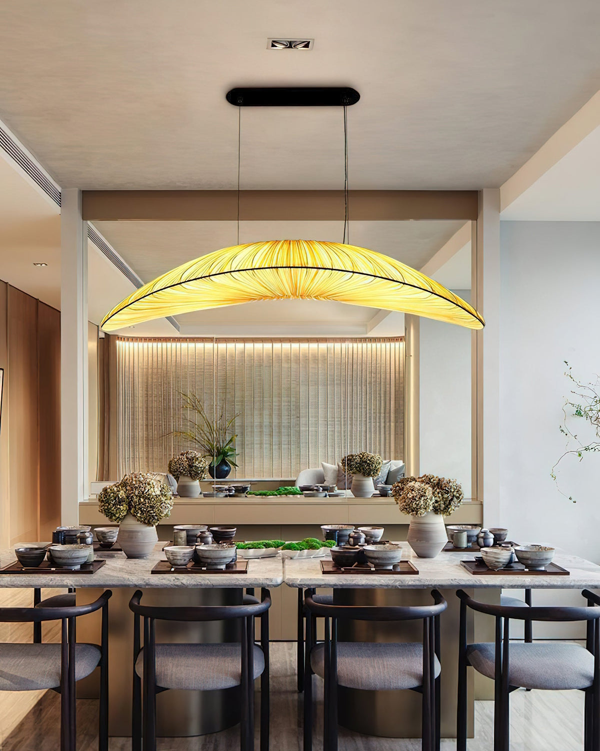 A Clérachic pendant lights a long dining table set with bowls and dishes, in a room with a softly lit wooden slatted wall.