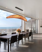 A Clérachic pendant in an amber glow hangs over a long dark dining table, with a wide glass wall and the sea in view.