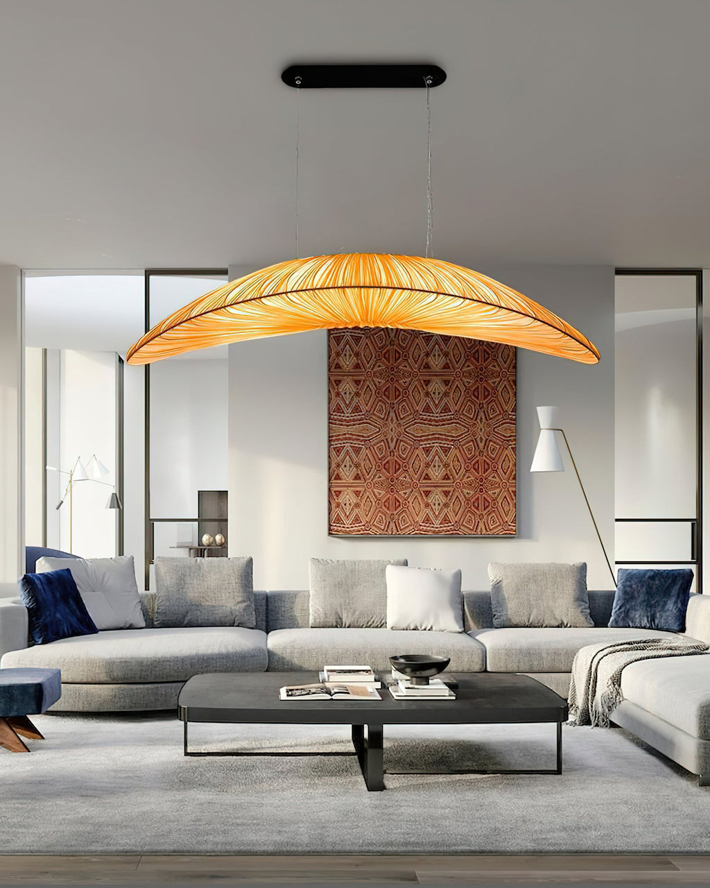 A Clérachic pendant with an amber shade hangs above a grey sofa and dark coffee table, in front of a rust-patterned wall hanging.