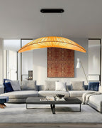 A Clérachic pendant with an amber shade hangs above a grey sofa and dark coffee table, in front of a rust-patterned wall hanging.