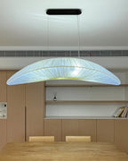 A Clérachic pendant with a cool bluish-white glow hangs in front of a built-in wooden cabinet, above a pale dining table.