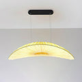 A Clérachic pendant with a black oval ceiling plate and a pale pleated shade that glows yellow in the middle, against a plain wall.