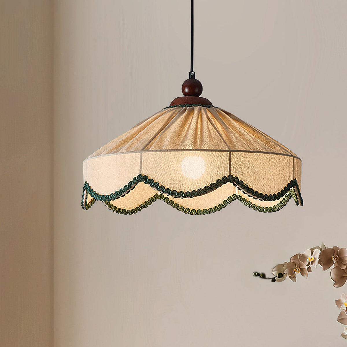 Clérachic pendant with a pleated beige shade and walnut finial, hung against a warm beige wall with orchid blooms at the edge.