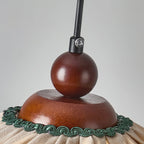 Close view of the walnut wooden ball, dome and black cord grip at the top of this Clérachic pendant, with green trim below.
