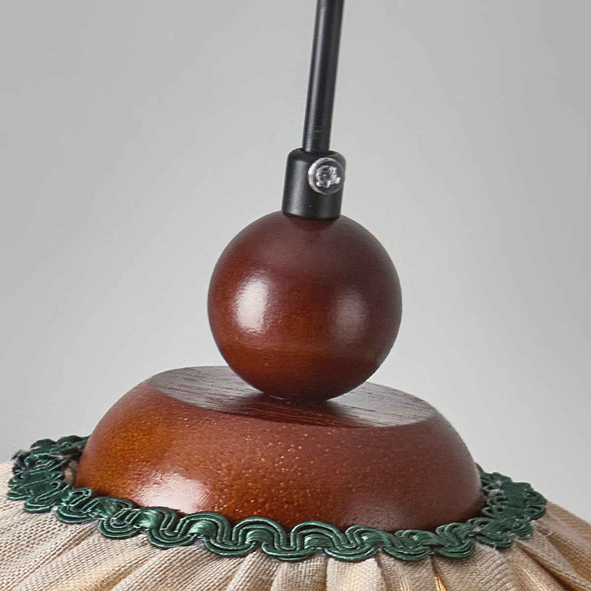 Close view of the walnut wooden ball, dome and black cord grip at the top of this Clérachic pendant, with green trim below.