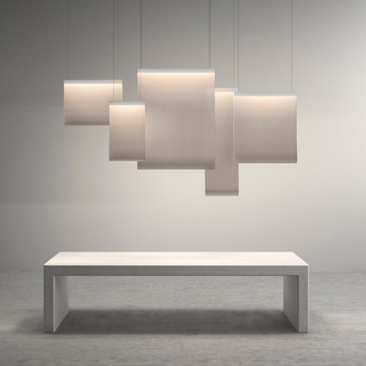 Five Clérachic fabric pendants of different sizes overlapping in a cluster above a pale stone bench, on a soft grey backdrop.