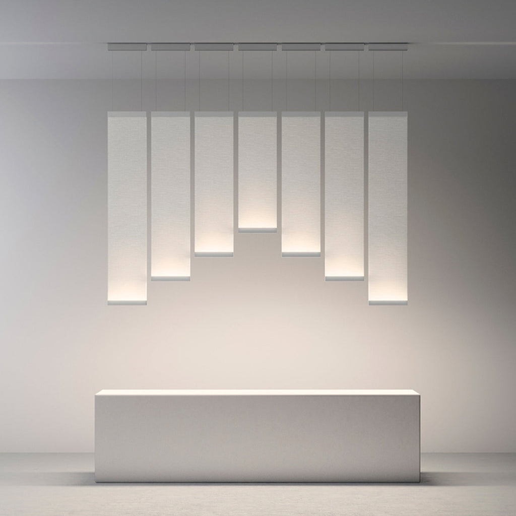 Seven Clérachic fabric panel pendants of graduated lengths lit in a row above a plain white block, on a pale grey wall.