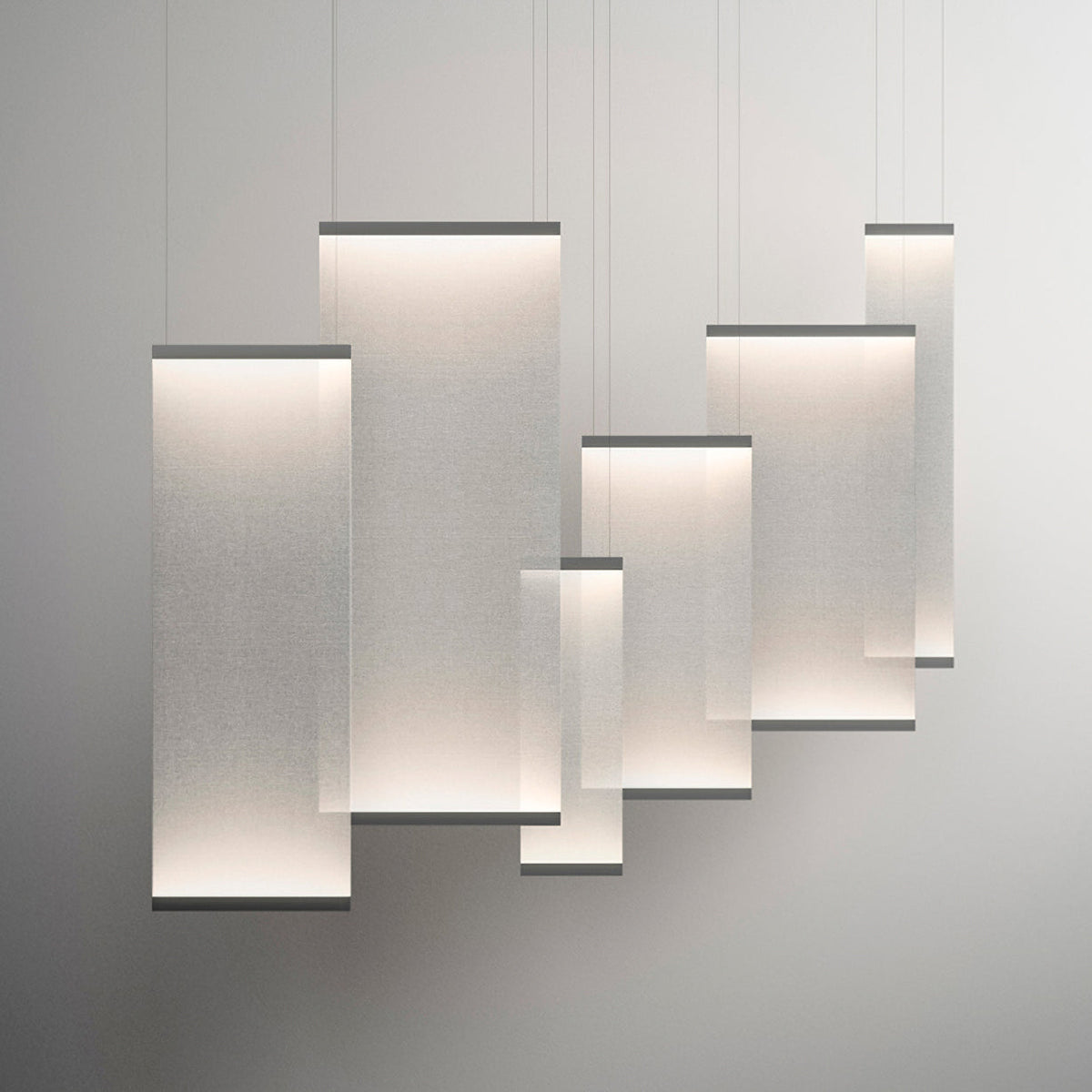 Six Clérachic fabric pendants of different sizes overlapping and lit, hung at varied heights against a pale grey backdrop.