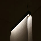 Close view of a Clérachic fabric panel curving down from a dark top bar, with a woven texture lit from the edge in a dark room.