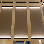 Three tall Clérachic fabric panels lit from a dark bar at the top, glowing down a plywood-framed wall.