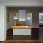Three Clérachic fabric pendants lit at different heights above a pine table, in a hall with dark floorboards and a framed painting.