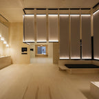 A line of tall Clérachic fabric panels lit along their top edges beneath a plywood ceiling, in a long open room.