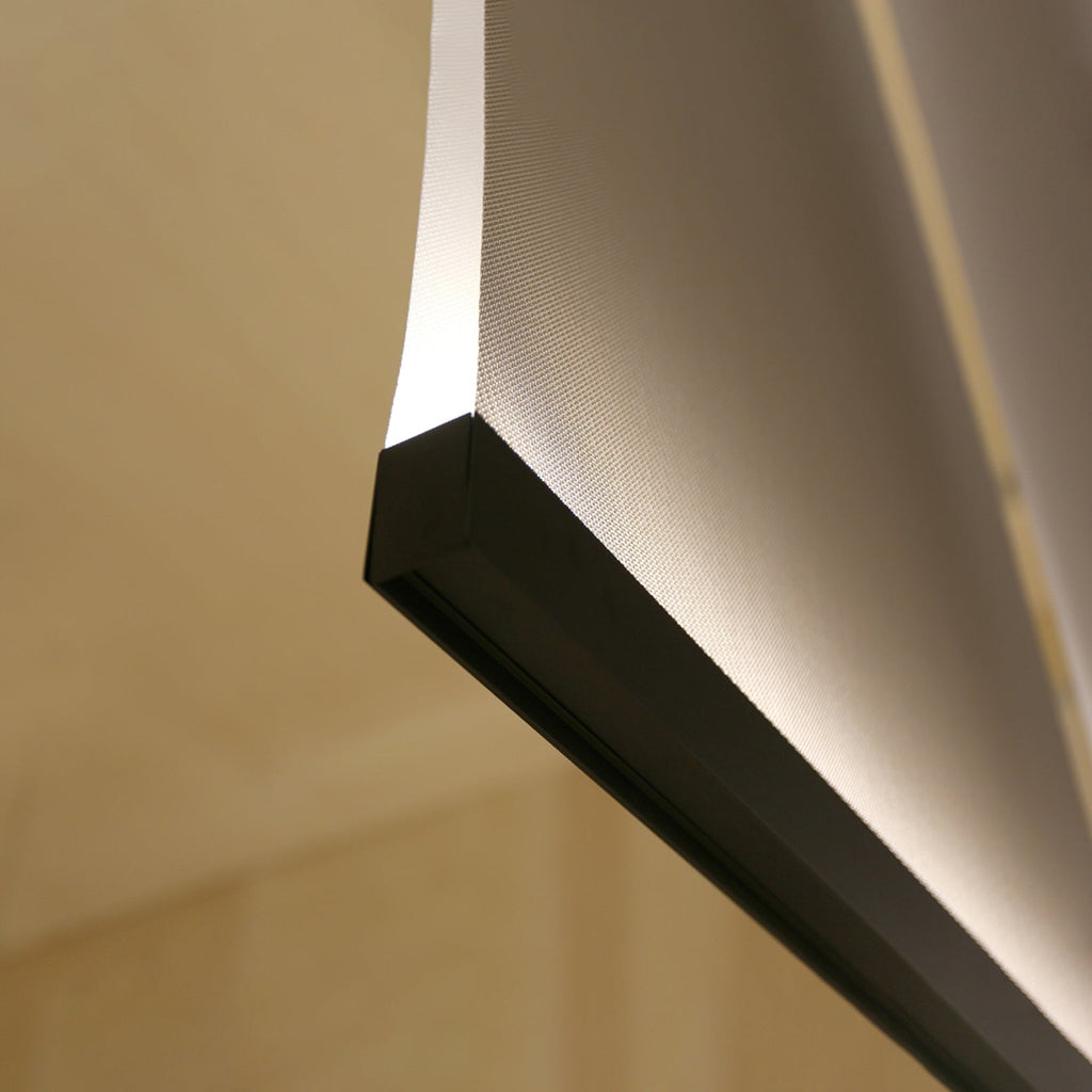 Close view of a Clérachic fabric panel curling above a black bar, with warm light along its edge against a wooden wall.