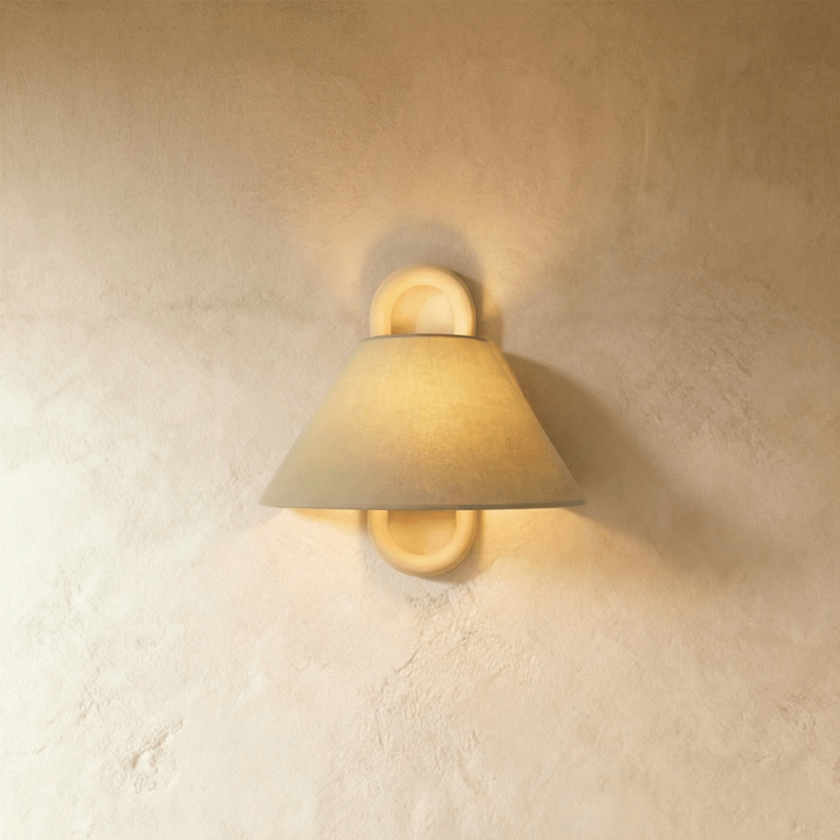 Clérachic wall light with a sage-toned fabric shade and solid wood ring mount, glowing warmly against a plaster bedroom wall.